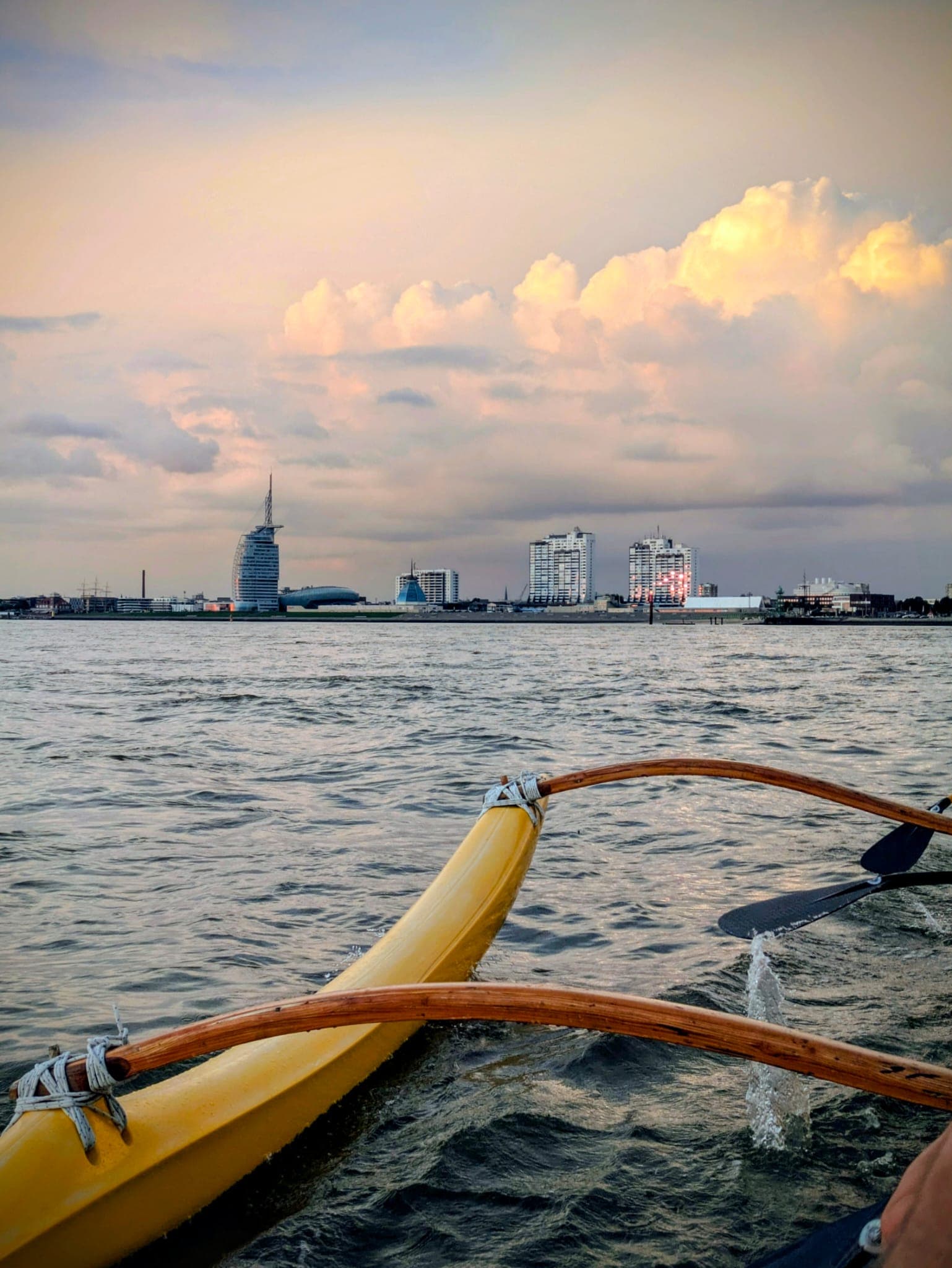 Blick aus einem Outrigger-Kanu auf die Skyline von Bremerhaven mit dem Atlantic Hotel Sail City bei Sonnenuntergang.
